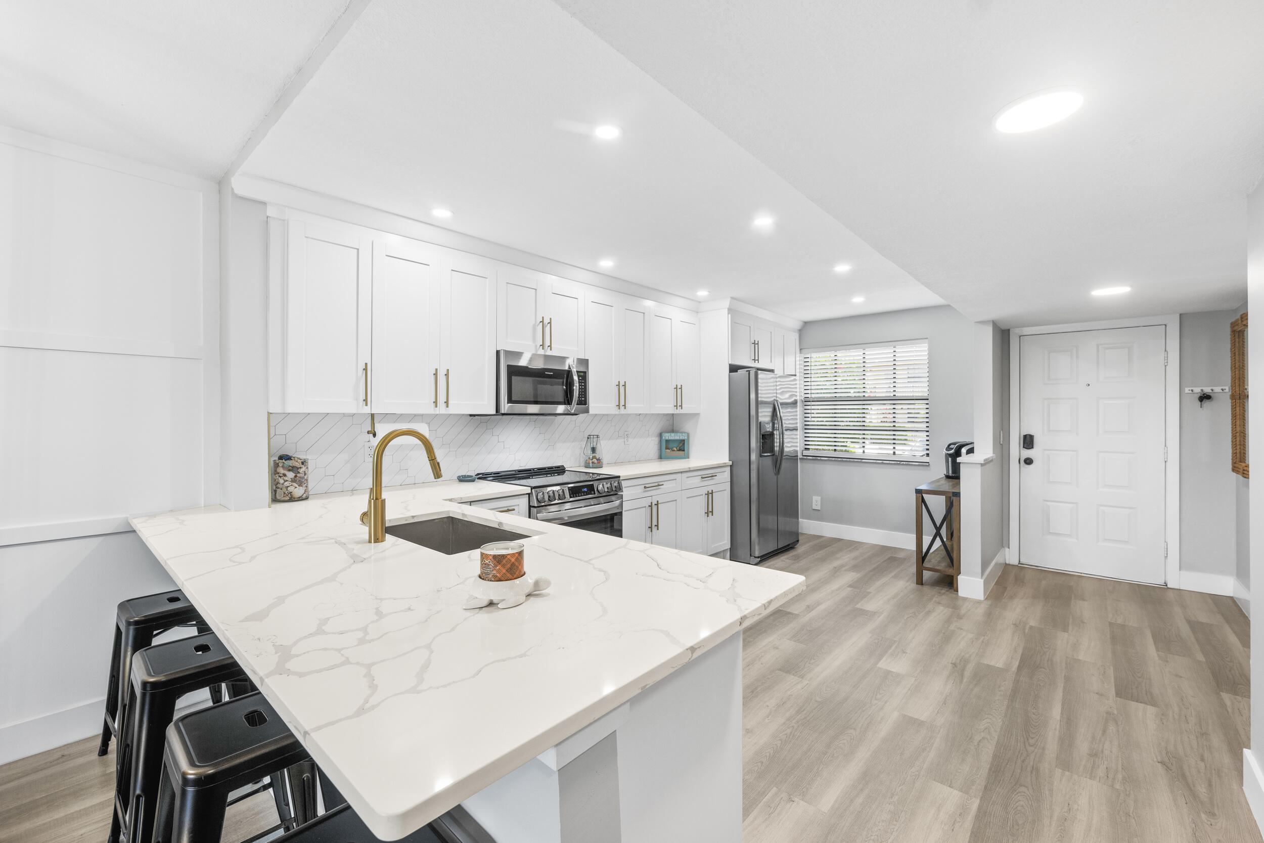 17867 Thelma Avenue, Unit A Jupiter, FL 33458 - Photo 3 of 35 a kitchen with stainless steel appliances kitchen island granite countertop a refrigerator a sink a stove and white cabinets with wooden floor