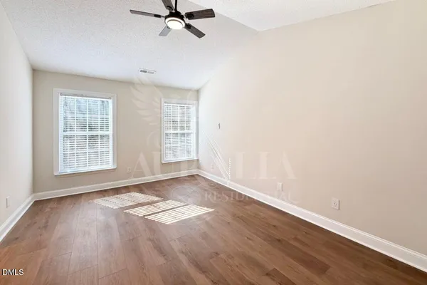 an empty room with wooden floor fan and windows