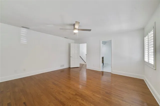 an empty room with wooden floor ceiling fan and windows