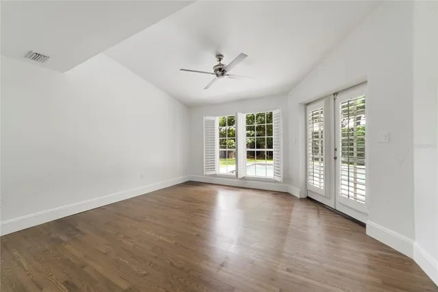 an empty room with wooden floor chandelier fan and windows