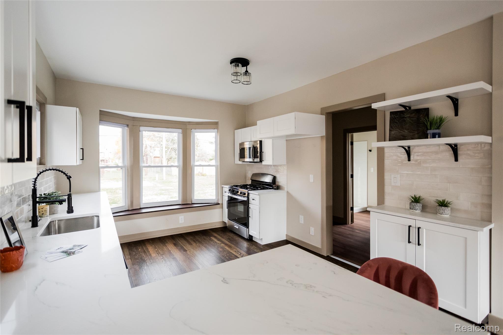 2630 Harding Street Detroit, MI 48214 - Photo 8 of 30 Renovated kitchen featuring white cabinetry, light-toned countertops, a stainless steel sink with a matte black faucet, wood-finish flooring, and a bay window