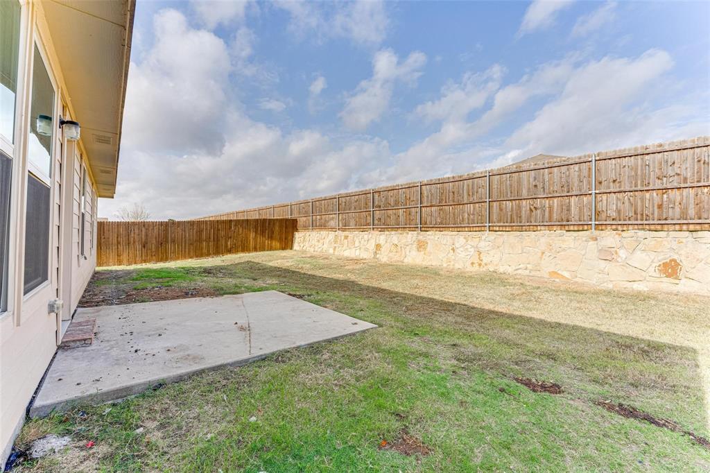 517 Milo Way Royse City, TX 75189 - Photo 26 of 34 Expansive grassy yard featuring a concrete patio, a wood privacy fence, and a stone retaining wall