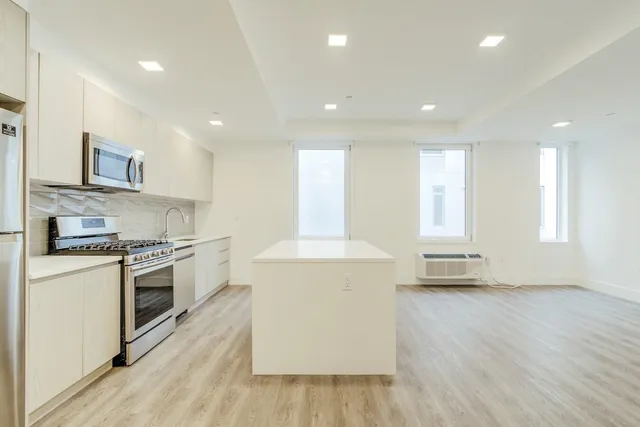 a kitchen with stainless steel appliances a stove a refrigerator a sink and white cabinets with wooden floor