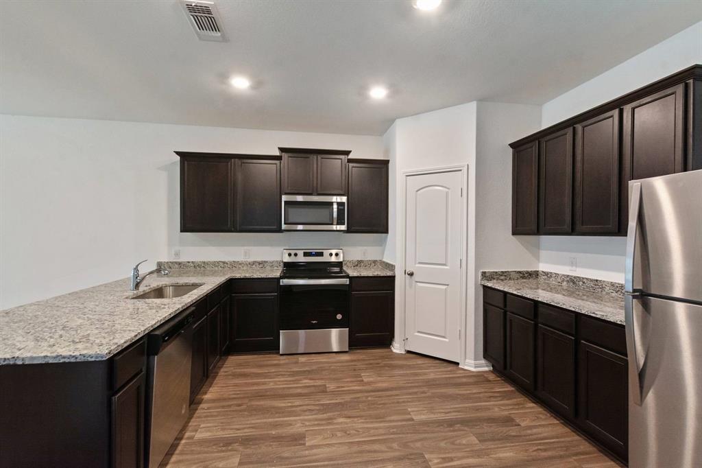16429 Farmhouse Lane Elgin, TX 78621 - Photo 7 of 22 Modern kitchen featuring dark wood cabinetry, light-toned countertops, stainless steel appliances, and wood-finish flooring