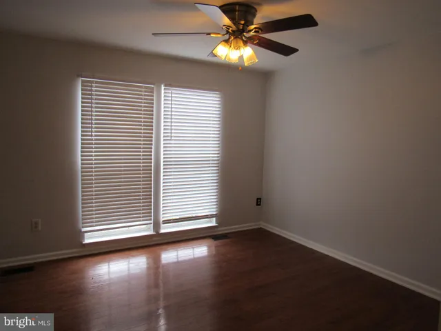 an empty room with wooden floor chandelier fan and windows