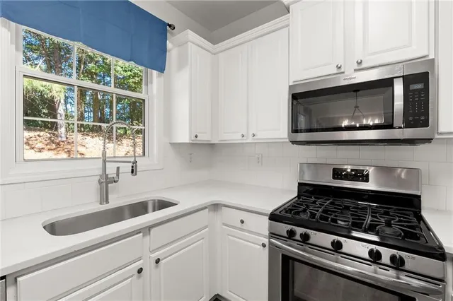 a kitchen with granite countertop white cabinets stainless steel appliances a sink and a window