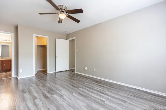 an empty room with wooden floor ceiling fan and windows