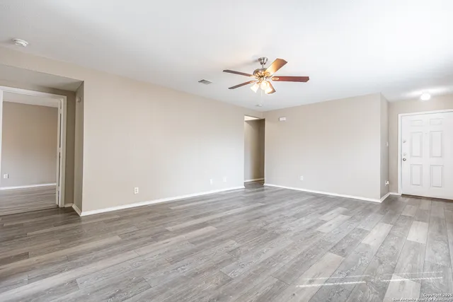 a view of an empty room with wooden floor and a ceiling fan