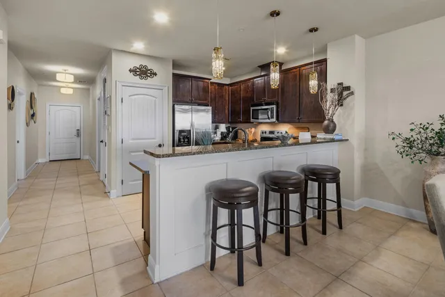 a kitchen with stainless steel appliances a sink a stove a refrigerator cabinets and chairs