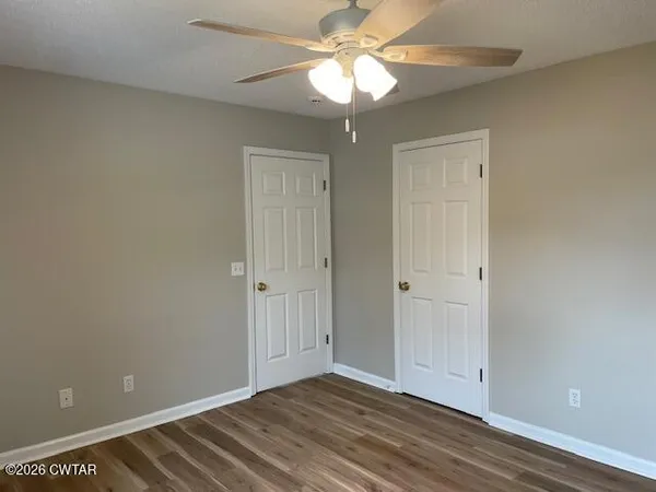 a view of an empty room with chandelier fan and wooden floor