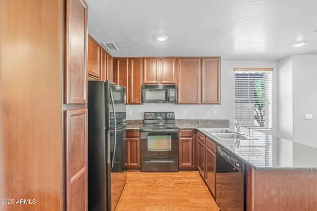 a kitchen with stainless steel appliances granite countertop a refrigerator a sink dishwasher and wooden cabinets with wooden floor