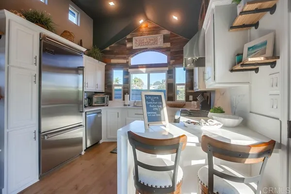 a kitchen with stainless steel appliances granite countertop a refrigerator a sink dishwasher a dining table and chairs with wooden floor