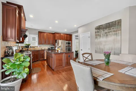 a kitchen with granite countertop a stove a sink a refrigerator and a dining table with wooden floor