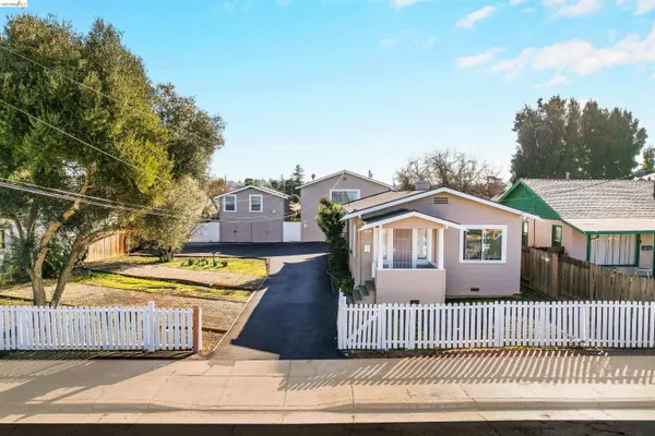 a view of a white house with a small yard and large trees