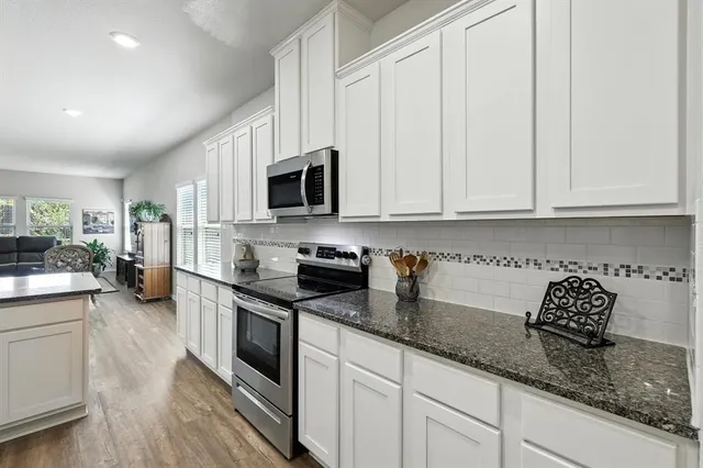 a kitchen with stainless steel appliances granite countertop a refrigerator a sink dishwasher a stove and white countertops with wooden floor