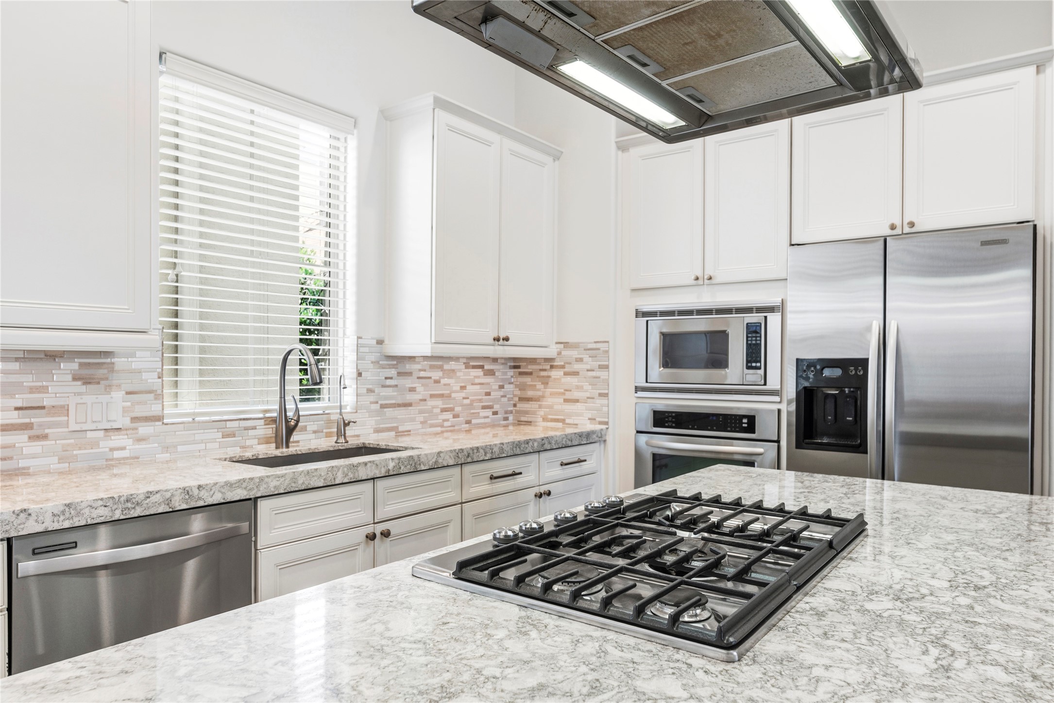 1537 Haddon Street Houston, TX 77006 - Photo 18 of 48 This modern kitchen features sleek stainless steel appliances, a spacious island with a gas cooktop, elegant granite countertops, and white cabinetry with a stylish tile backsplash. The large window provides ample natural light.