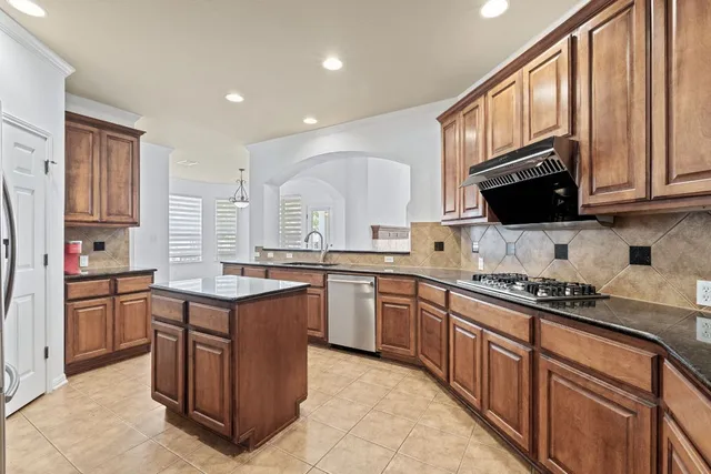 a kitchen with stainless steel appliances granite countertop a stove top oven a sink dishwasher and a refrigerator with wooden cabinets