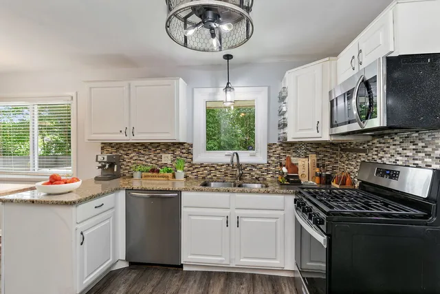 a kitchen with stainless steel appliances granite countertop a sink dishwasher a stove a microwave oven and a dining table with wooden floor