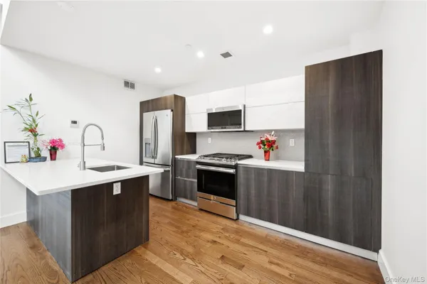 a kitchen with stainless steel appliances a sink dishwasher a refrigerator and a stove with wooden floor