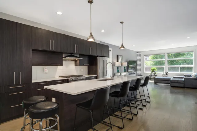 a kitchen with stainless steel appliances granite countertop a stove a refrigerator a sink a dining table and chairs with wooden floor