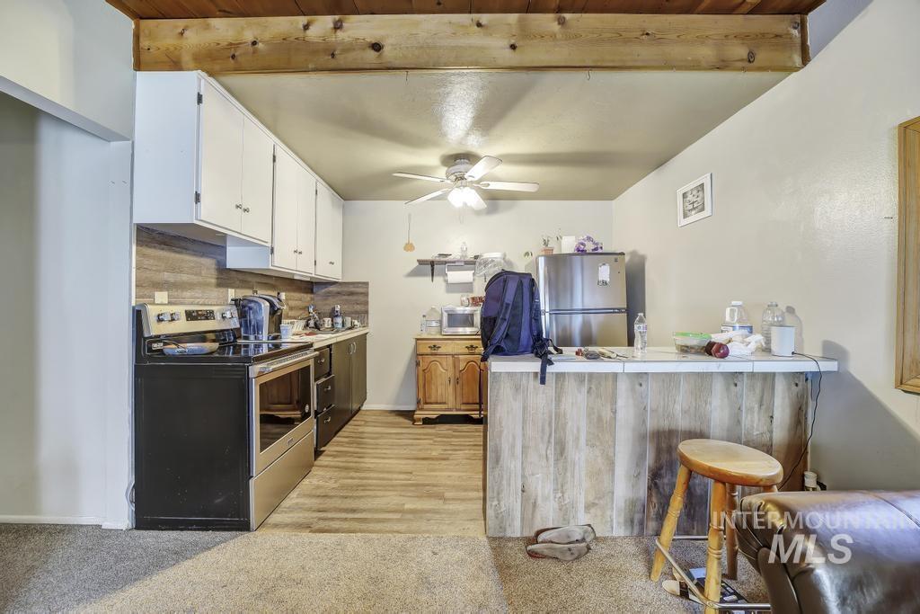 111 2nd Street Rupert, ID 83350 - Photo 26 of 45 Kitchen area featuring a wood-finish ceiling beam, white upper cabinetry, stainless steel appliances, wood-look flooring, and a breakfast bar with a wood-plank facade