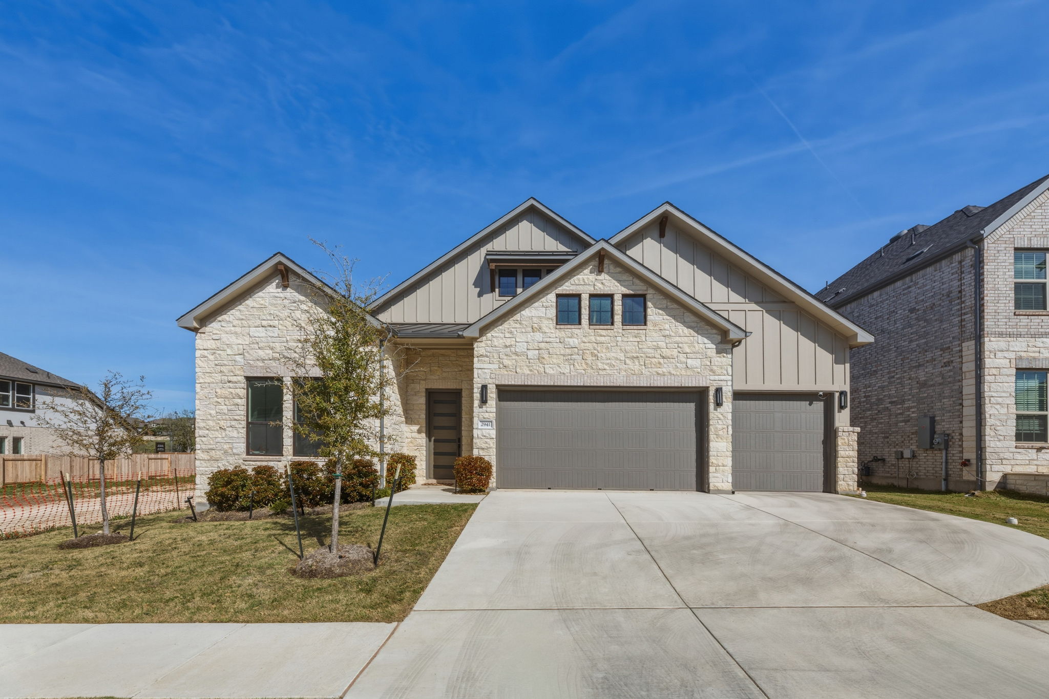 View of front facade with board and batten siding, stone siding, concrete driveway, a standing seam roof, and an attached garage