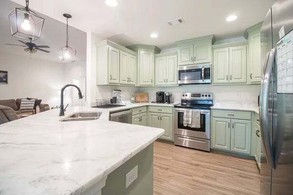 a kitchen with stainless steel appliances granite countertop a sink a stove a refrigerator cabinets and a kitchen island with wooden floor