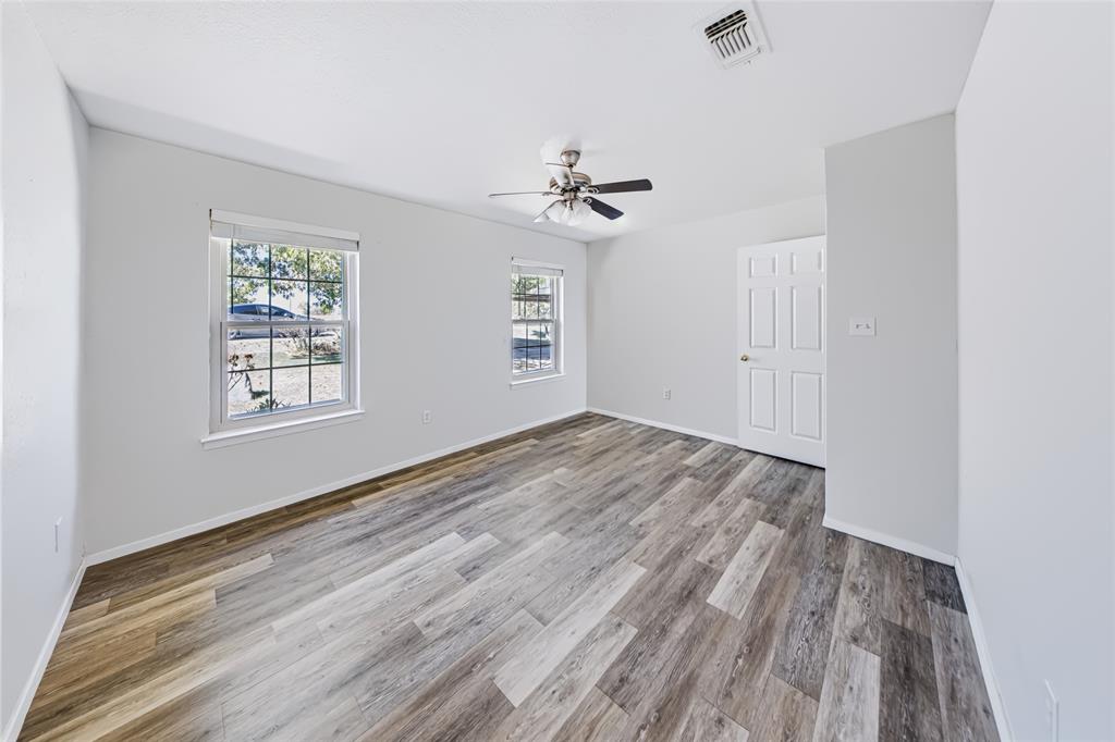 560 Green Acres Road Weatherford, TX 76088 - Photo 12 of 35 Main home — second bedroom. Wood-finish flooring, two large windows, overhead ceiling fan, and a paneled door