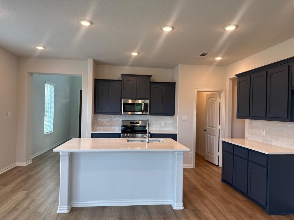 1233 Frio Drive Springtown, TX 76082 - Photo 4 of 13 Contemporary kitchen featuring a center island with sink, dark blue cabinetry, light tile backsplash, and wood-finish flooring