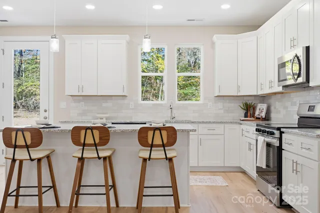 a kitchen with stainless steel appliances granite countertop a stove a sink dishwasher and white cabinets with wooden floor