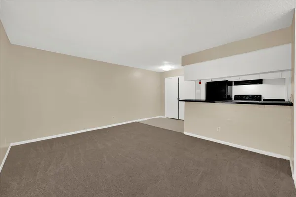 a view of an empty room with kitchen and microwave