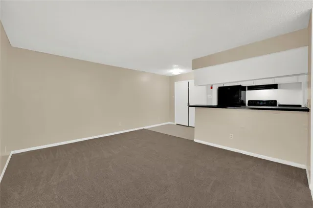 a view of an empty room with kitchen and microwave