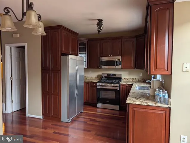 a kitchen with granite countertop wooden cabinets a stove top oven a refrigerator and a sink