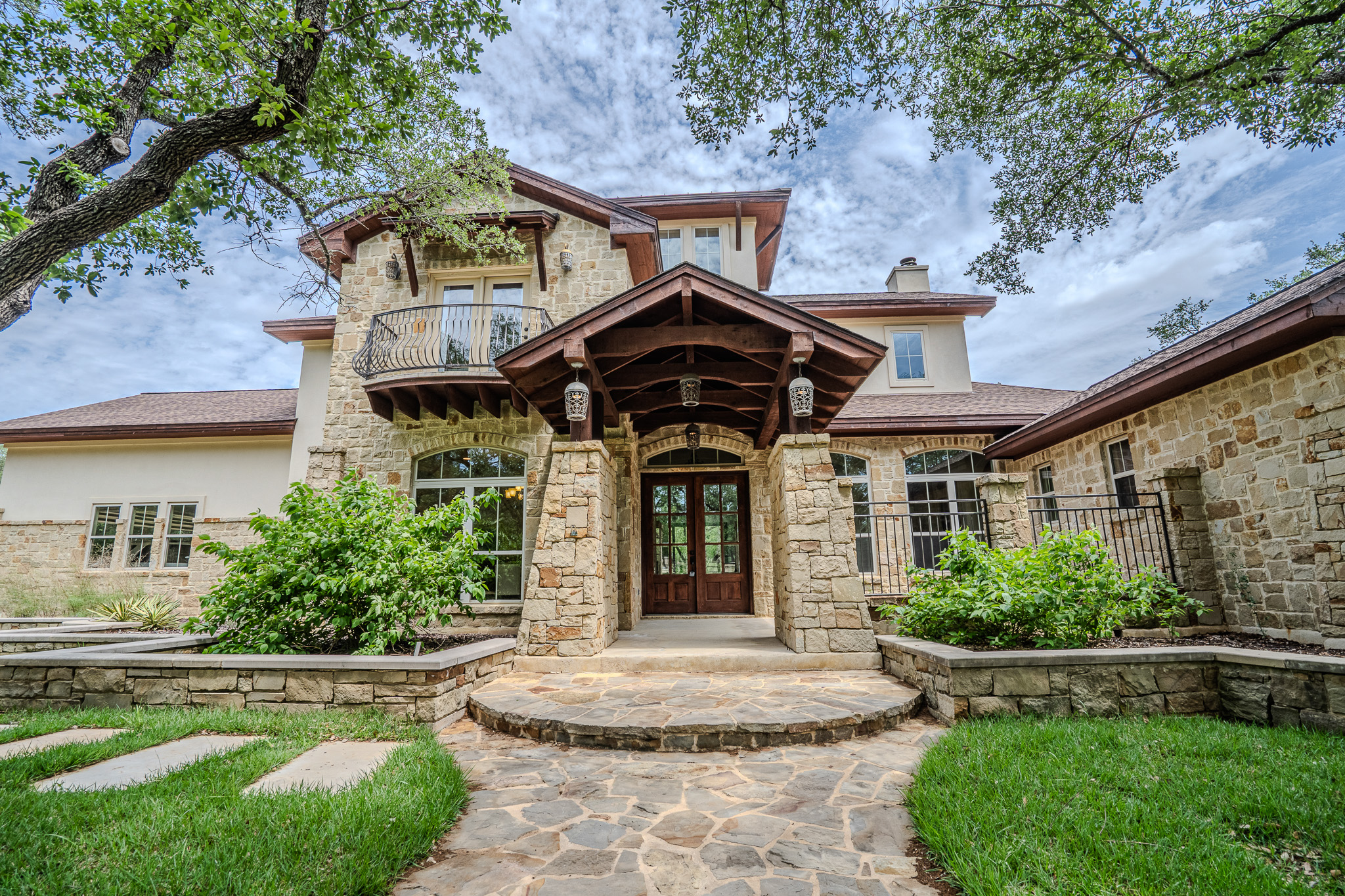 Stone exterior with a covered entry, double wooden doors, second-story balcony with iron railing, and a stone walkway