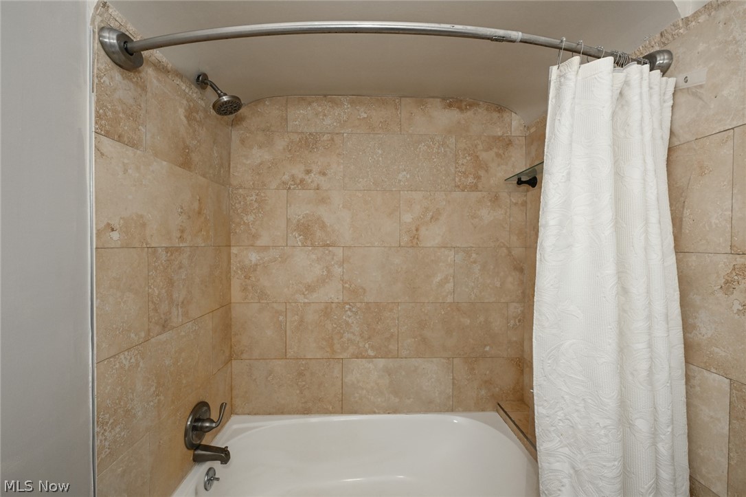 3699 Bainbridge Road Cleveland Heights, OH 44118 - Photo 31 of 37 Bathtub and shower combination featuring neutral-toned tile surround, a built-in shelf, and a curved shower rod