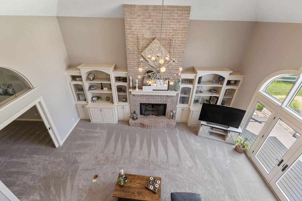 2570 Jewett Road Powell, OH 43065 - Photo 16 of 104 • New grey carpet ~ 2022 • Grey/tan painted walls • Two story ceiling • Can lighting • Chandelier • Brick fireplace with mantle, raised hearth, & gas logs • Built-in bookcases • Large window • French doors to Composite Deck
