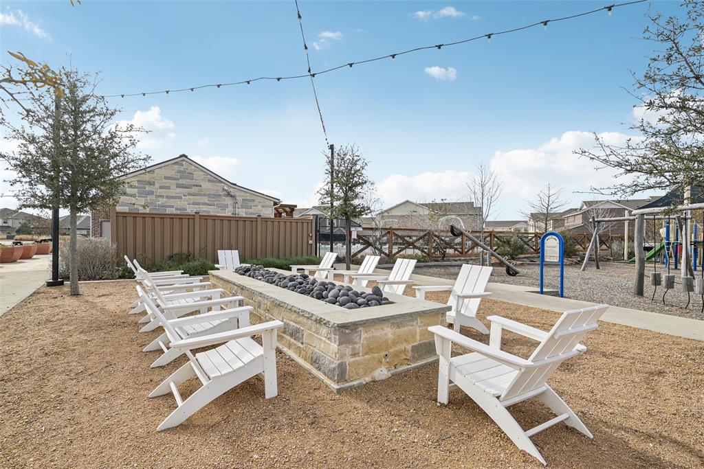 4430 Prairie Crossing Prosper, TX 75078 - Photo 5 of 15 Outdoor amenity area featuring a stone-clad fire pit with decorative rocks, surrounded by white Adirondack chairs