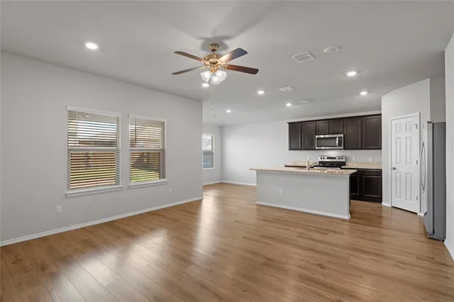 a view of an empty room with chandelier fan and wooden floor