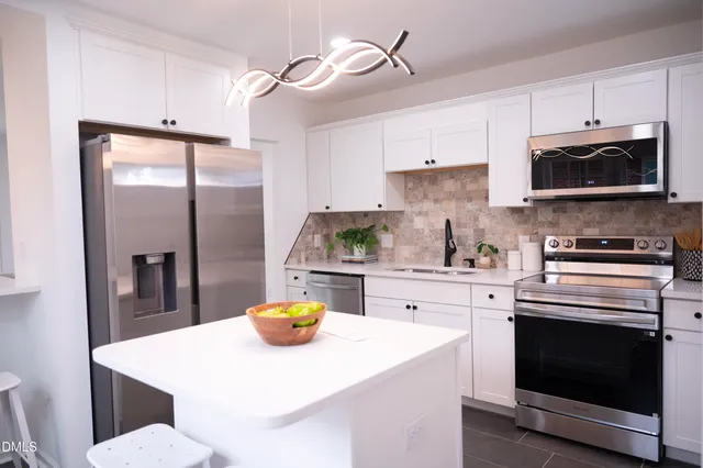 a kitchen with stainless steel appliances a stove a sink a refrigerator cabinets and dining table