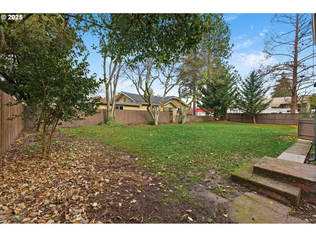 a view of a backyard with large trees and wooden fence