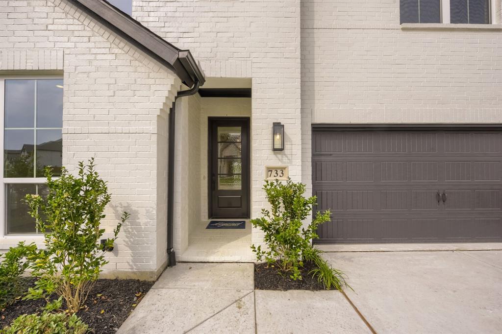 733 Red Cedar Road Haslet, TX 76052 - Photo 2 of 28 White brick exterior featuring a dark paneled entry door with glass inserts, a single exterior sconce, and an attached garage with a dark sectional door