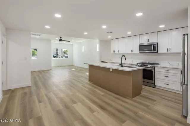 a kitchen with stainless steel appliances granite countertop a sink dishwasher a stove and a refrigerator with wooden floor