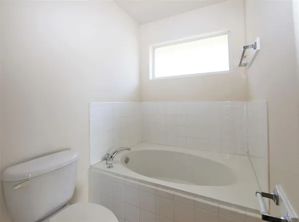 a bath tub sitting next to a white toilet and a window