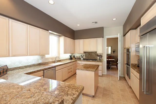 a large kitchen with kitchen island granite countertop a large counter top stainless steel appliances a sink cabinets and a window