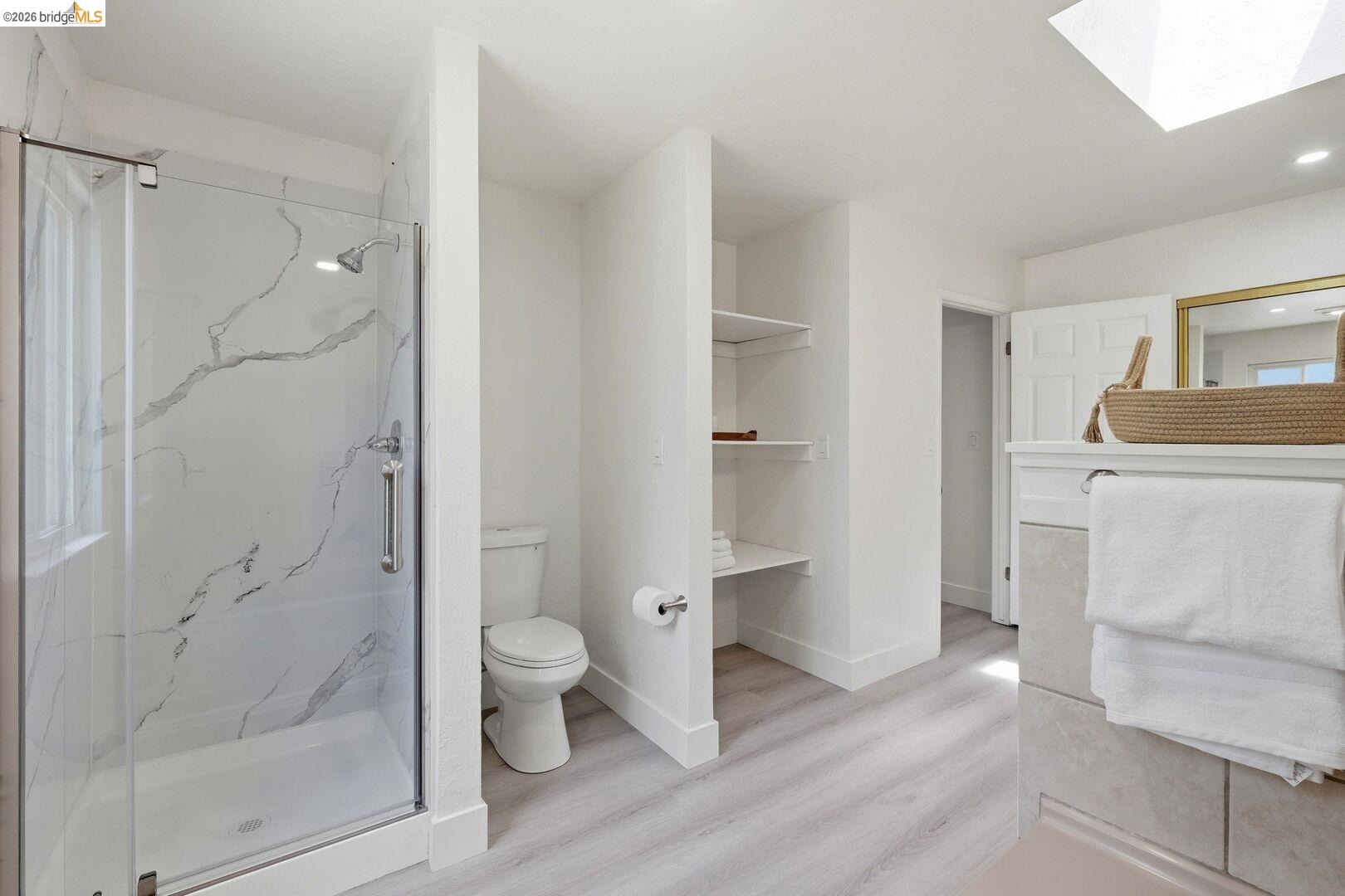 1590 Sunset Road Brentwood, CA 94513 - Photo 24 of 45 Modern master bathroom featuring a glass-enclosed shower with a marble-patterned surround, light wood-finish flooring, built-in shelving, a skylight, and a vanity with a mirror