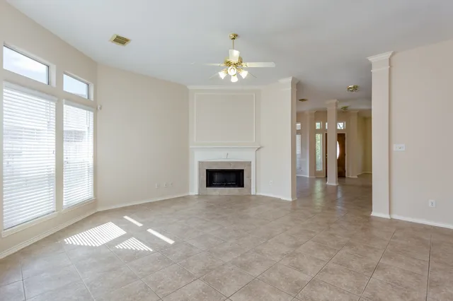 an empty room with chandelier fan and kitchen view