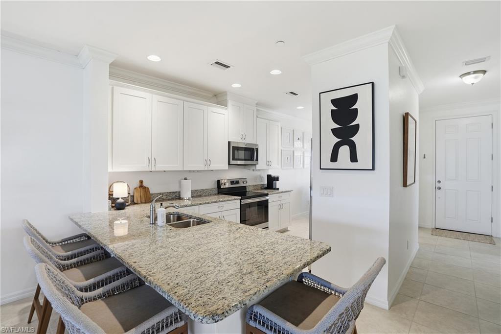 9374 Pocida Court, Unit 101 Naples, FL 34119 - Photo 10 of 32 a kitchen with stainless steel appliances kitchen island granite countertop a stove and white cabinets