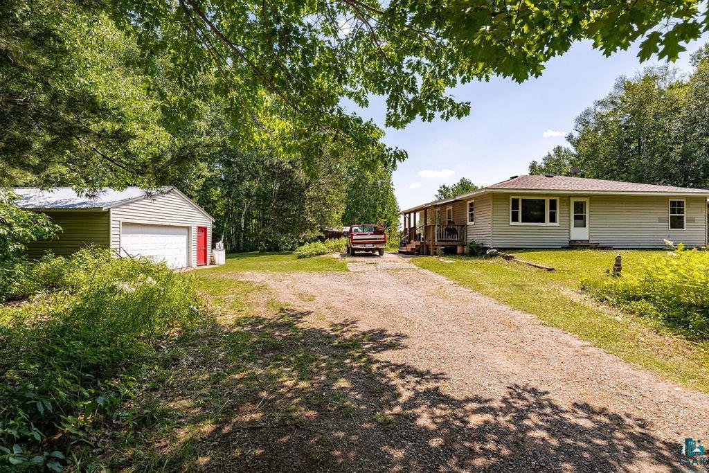 2592 Strandberg Road Barnum, MN 55707 - Photo 10 of 44 Property exterior featuring horizontal siding, a gravel driveway, a large detached garage with a white overhead door, and a covered porch