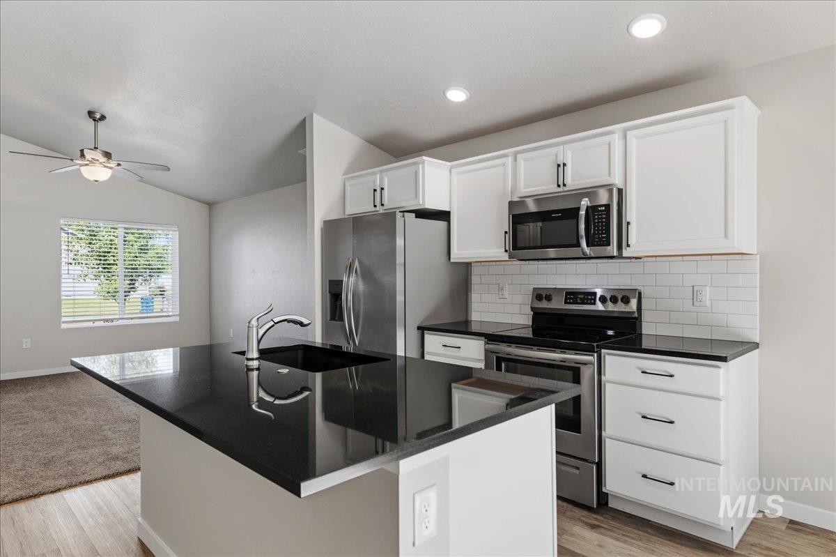 3091 S Green Boise, ID 83709 - Photo 10 of 27 Kitchen featuring a black countertop island with an integrated sink, white cabinetry, stainless steel appliances, and a subway tile backsplash