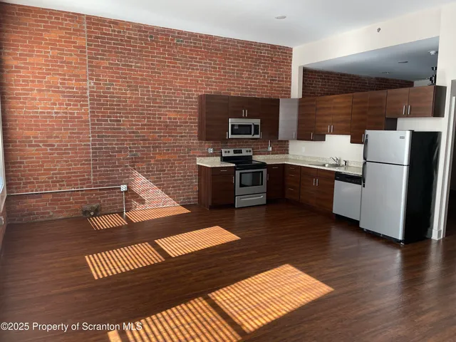a view of kitchen with stainless steel appliances wooden floor and living room view